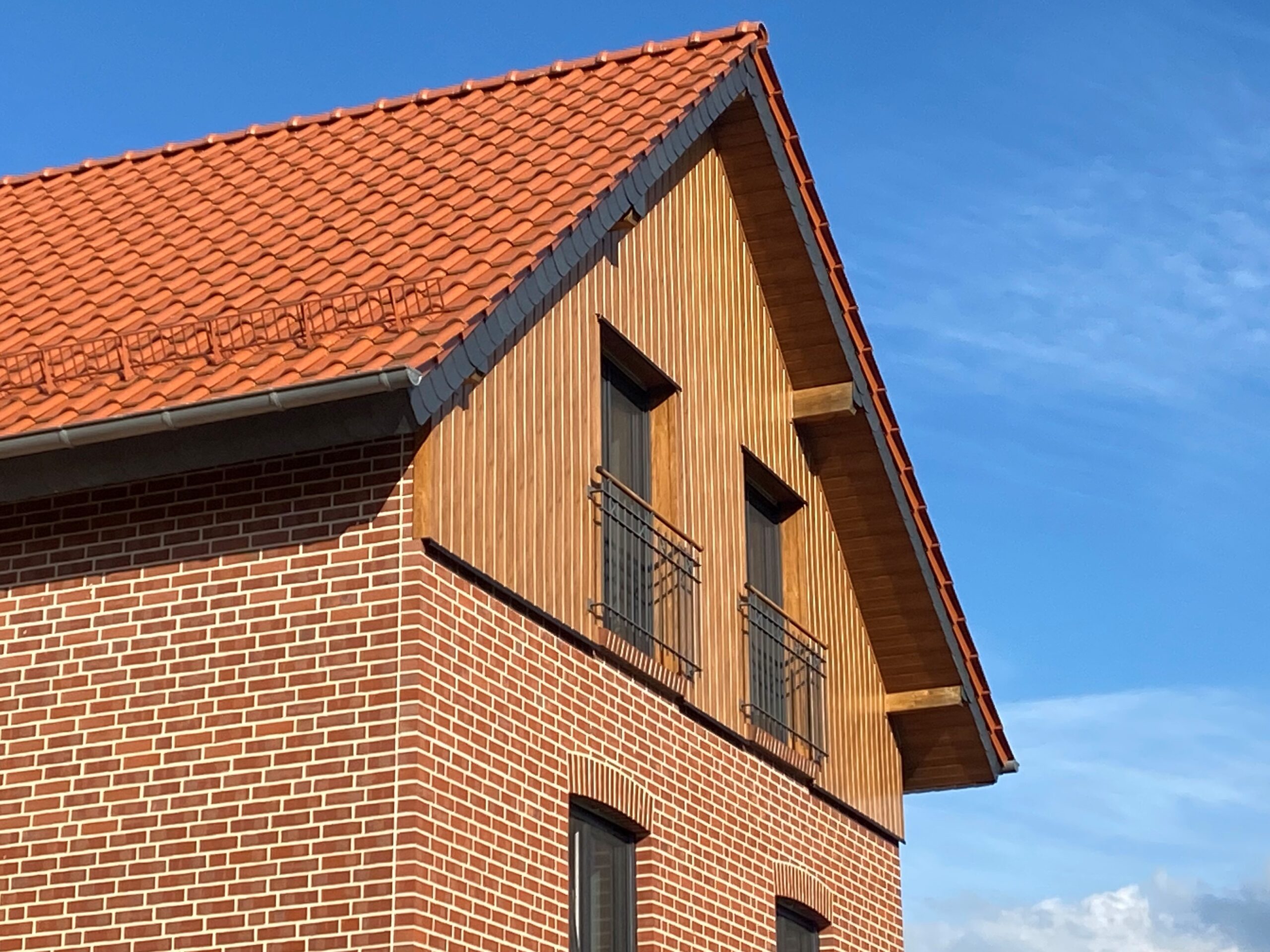 Teil eines Hauses mit rotem Ziegeldach und Fassade aus roten Backsteinen und Holzverkleidung, fotografiert bei blauem Himmel.