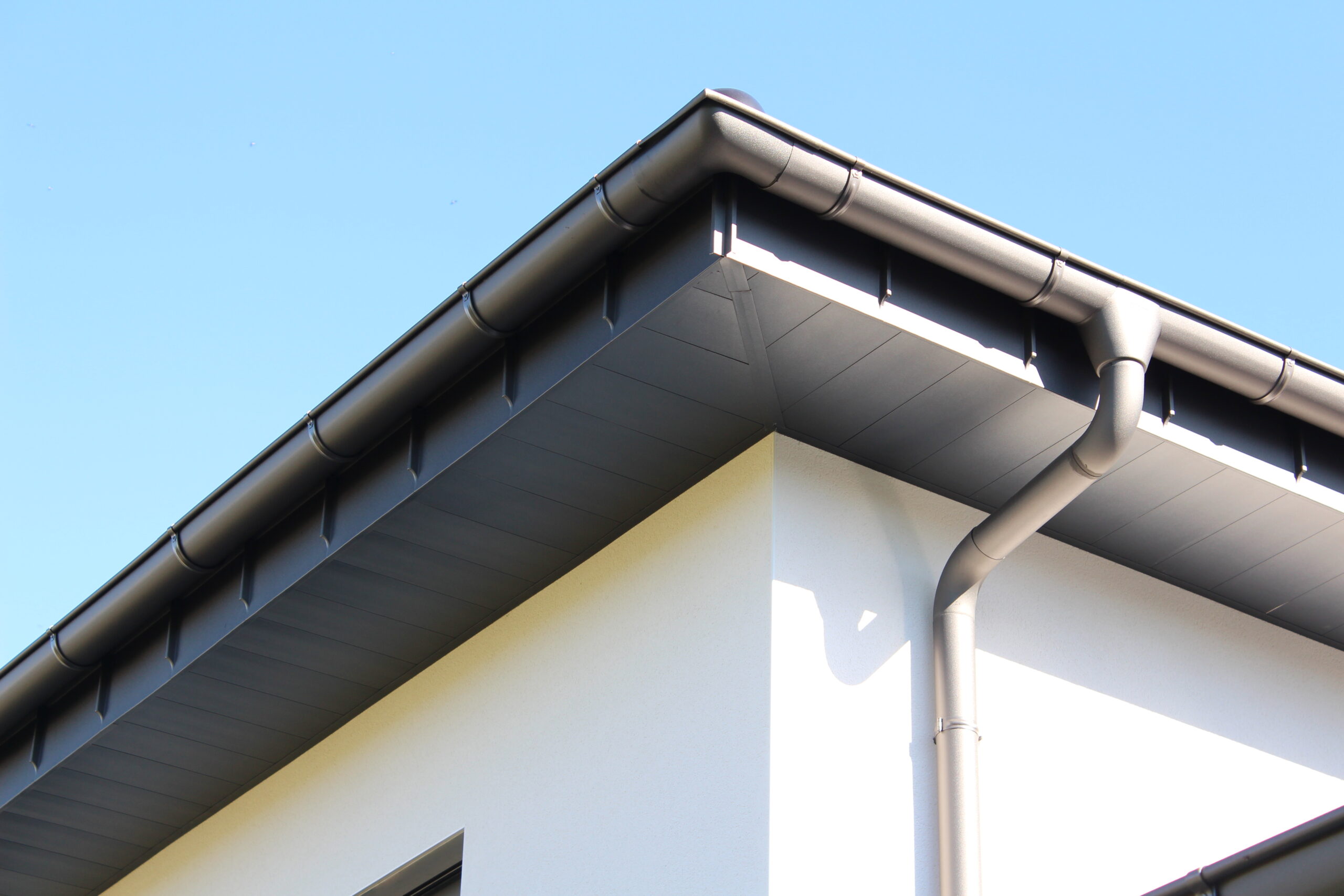 Nahaufnahme einer modernen Dachrinne und Fallrohr an einem Gebäude vor blauem Himmel.