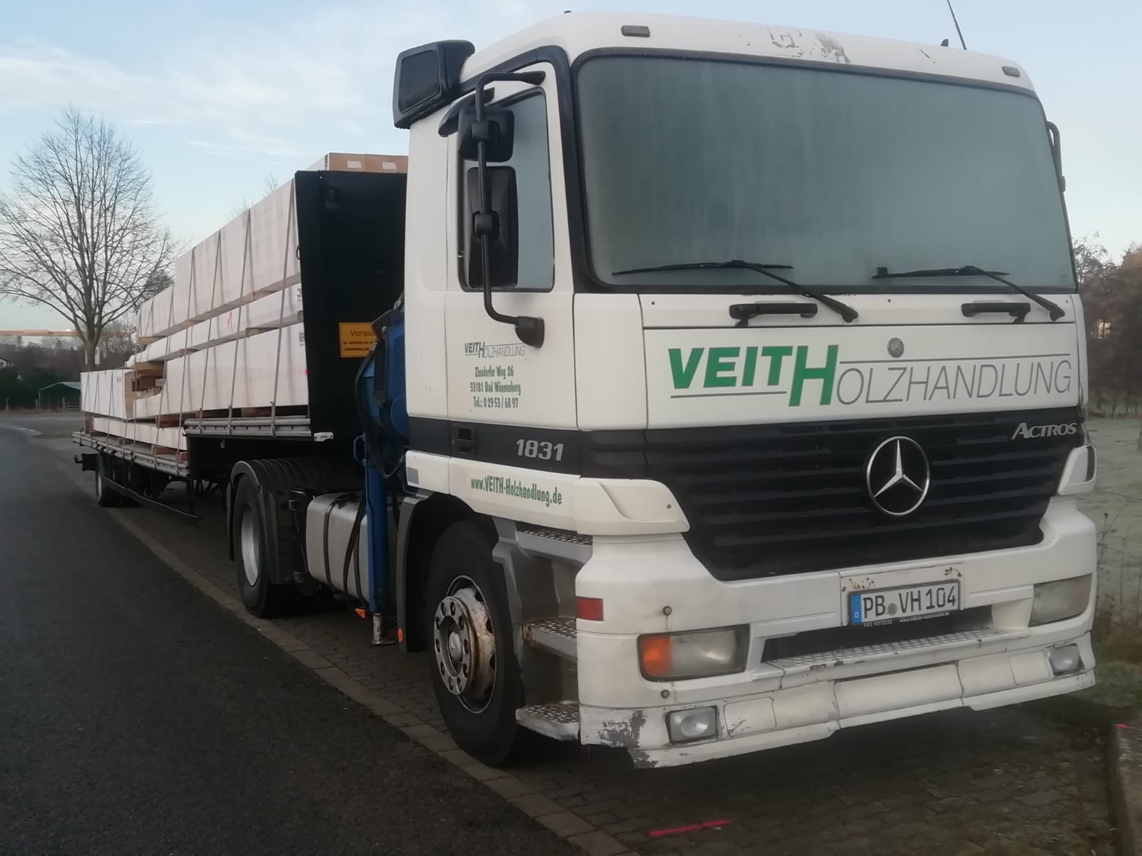 Ein Lastwagen der Marke Mercedes-Benz Actros, beschriftet mit "Veith Holzhandlung", steht auf einer Straße. Auf dem Anhänger sind große Pakete gestapelt.