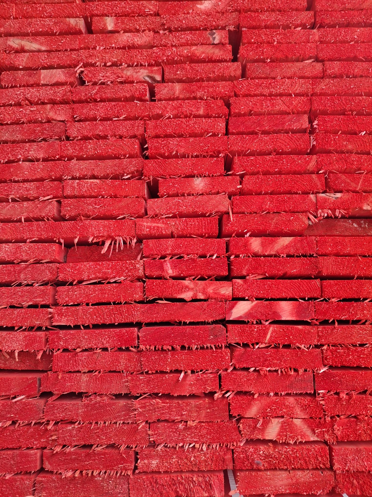 Ein Stapel roter, gespleißter Holzbretter, die eng übereinander gestapelt sind und eine raue, faserige Oberfläche aufweisen.