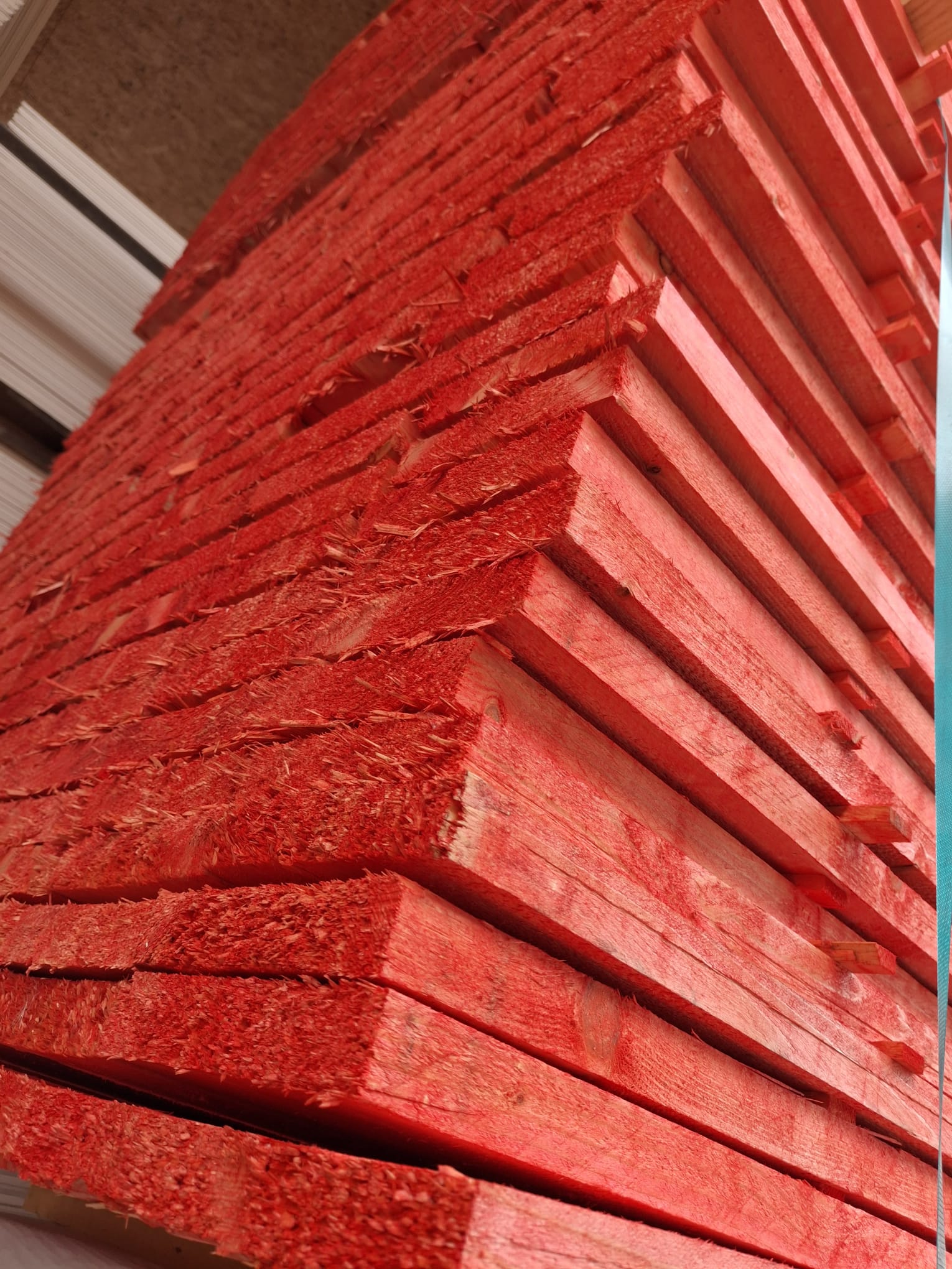 Ein Stapel roter Holzbretter, dicht gestapelt und schräg in der Nahaufnahme fotografiert, mit deutlich sichtbarer Maserung und rauen Kanten.