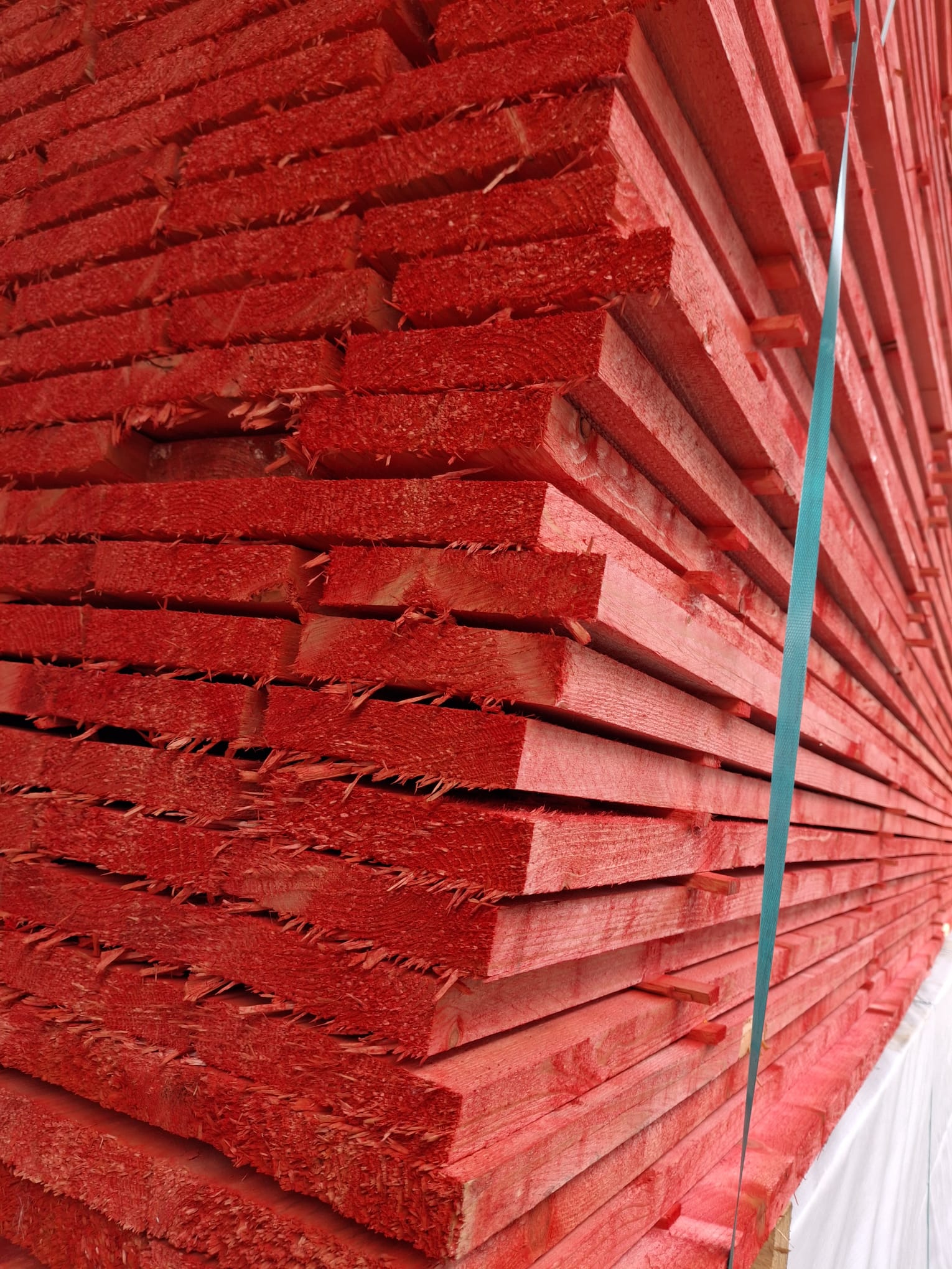 Ein Stapel von roten Holzlatten, die eng aufeinander geschichtet sind und mit einem blauen Gurt gesichert werden.