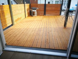 Holzterrasse mit Sichtschutz aus Holz und einem Grill im hinteren Bereich.