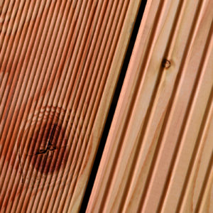 Nahaufnahme von holzfarbenen Terrassendielen mit feinen Rillen und einer Aststruktur.