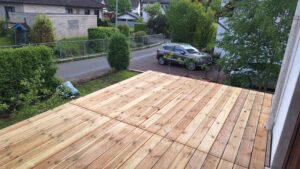 Eine neue Holzterrasse in einem Garten, mit einem Auto in der Einfahrt im Hintergrund.