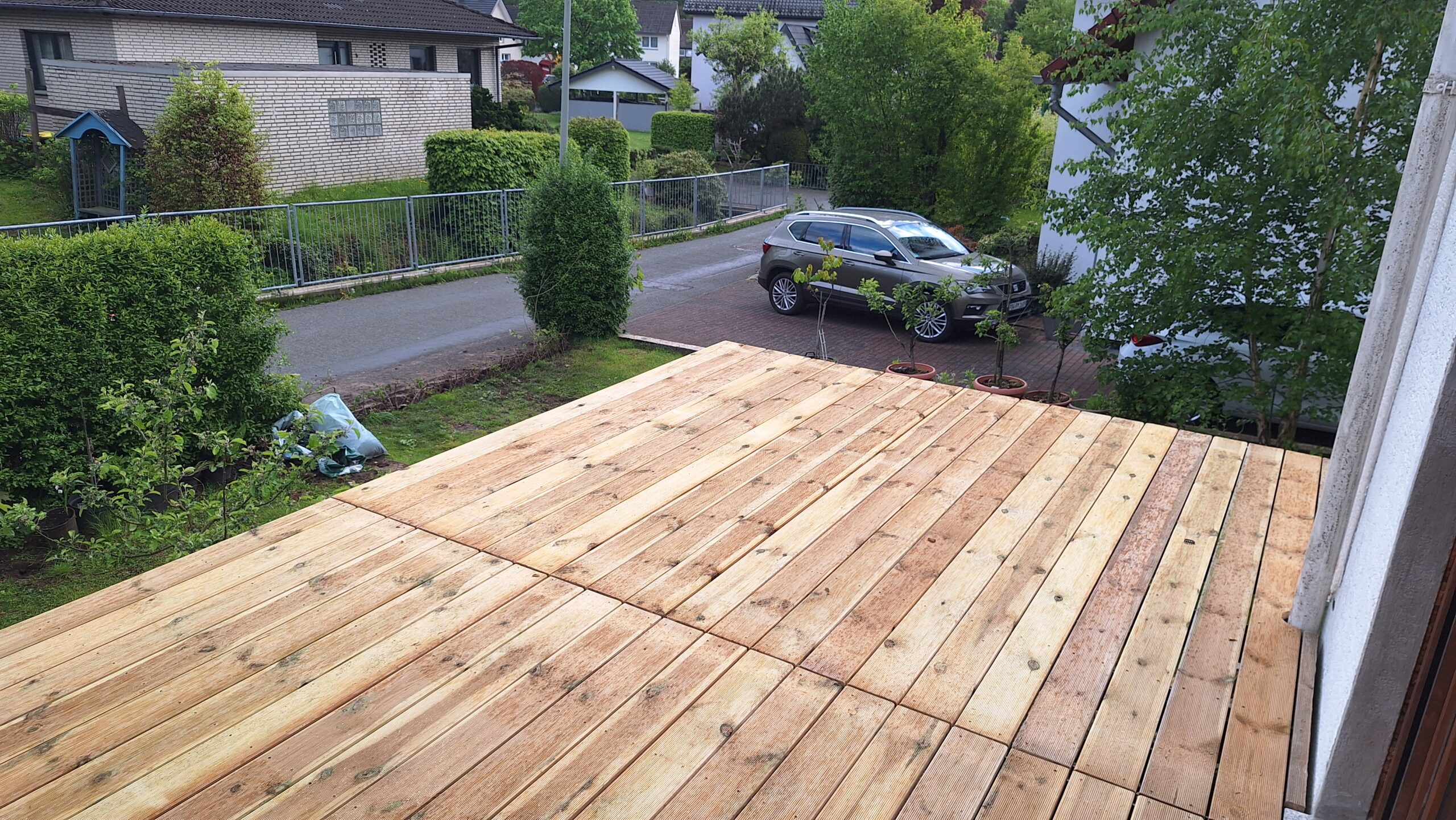 Eine neue Holzterrasse in einem Garten, mit einem Auto in der Einfahrt im Hintergrund.