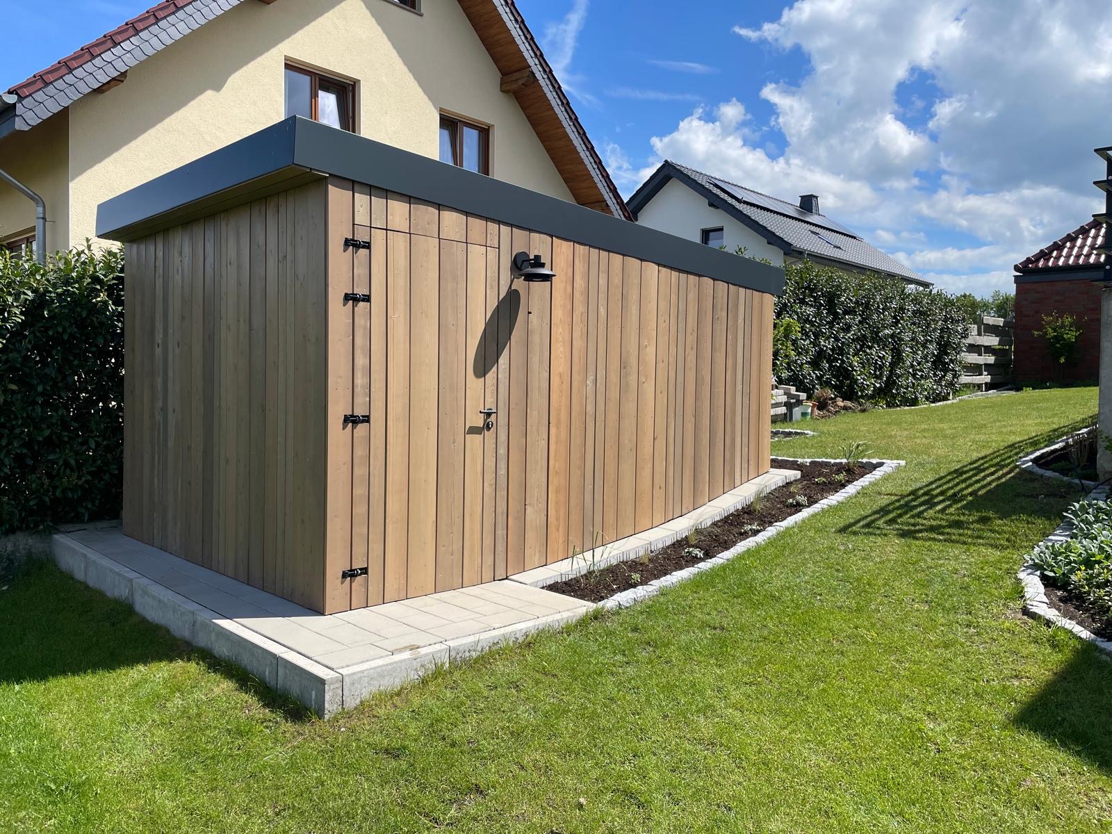 Holzschuppen im Garten, neben Wohnhäusern, bei sonnigem Wetter.