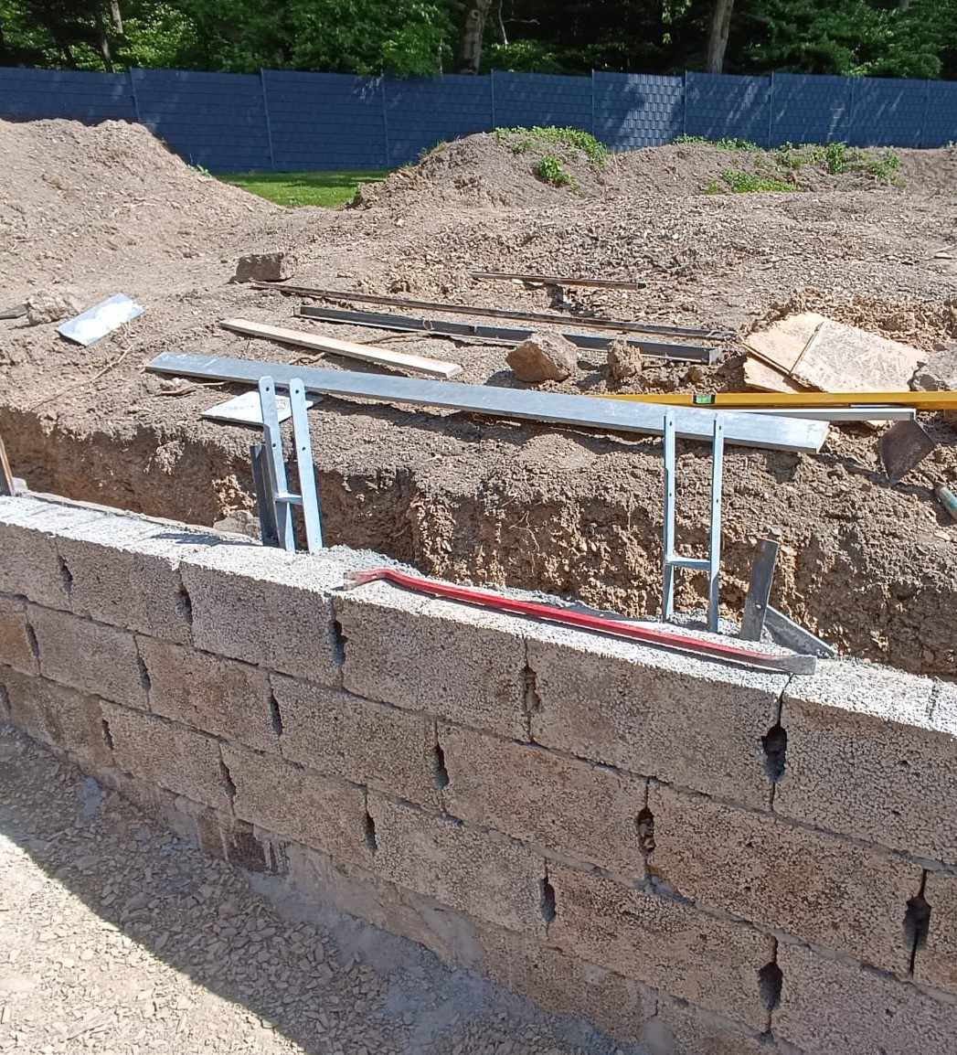 Unfertiger Mauerbau mit Betonblöcken und Bauwerkzeugen auf einer Baustelle.
